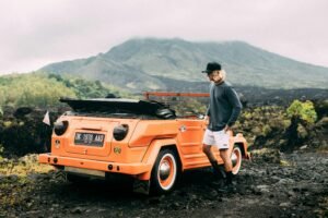A man with a vintage orange Volkswagen in scenic Bali landscape, perfect for travel inspiration.